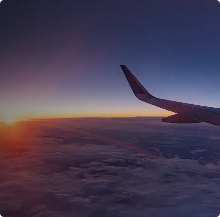 Airplane wing over a sunset or sunrise with clouds below