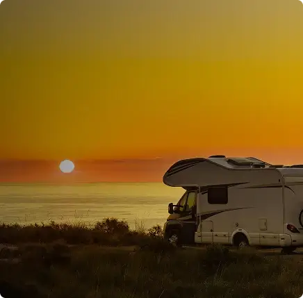 RV parked by a body of water with a sunset in the background